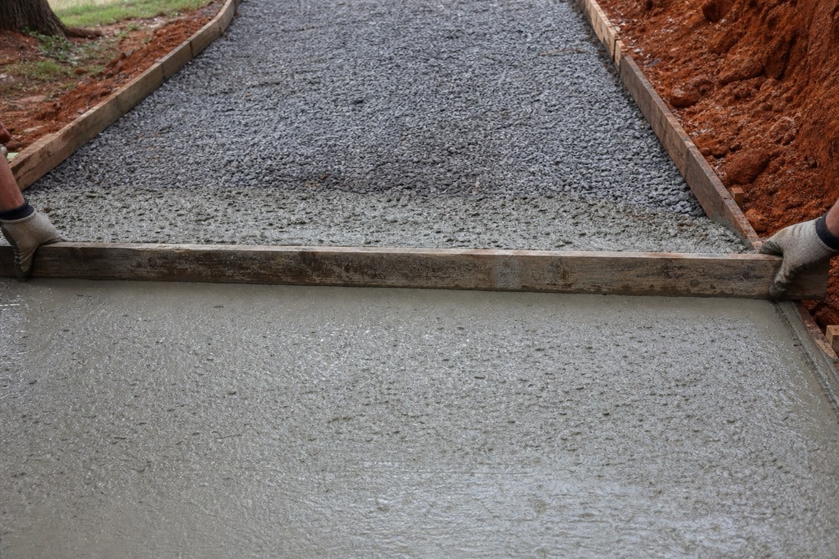 Concrete being screeded across a freshly poured residential driveway over a compacted gravel base