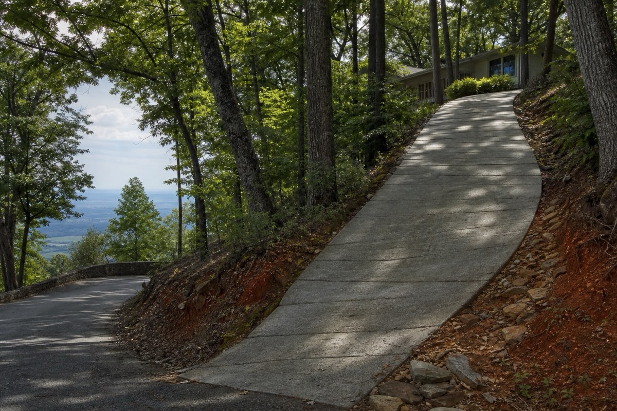 Steep broom-finished concrete driveway climbing a wooded hillside lot on Monte Sano